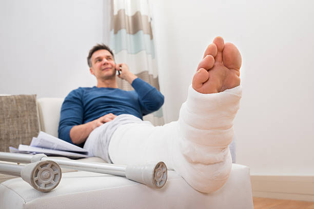 Disabled Man Talking On Cellphone Man With Fractured Leg Sitting On Sofa Talking On Cellphone man sitting with a bandage on his leg stock pictures, royalty-free photos & images