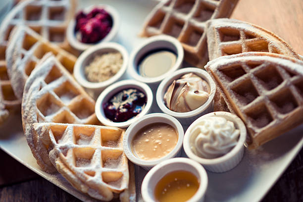 A close-up a waffle covered in maple syrup and a few strips of bacon.  A delicious weekend breakfast!