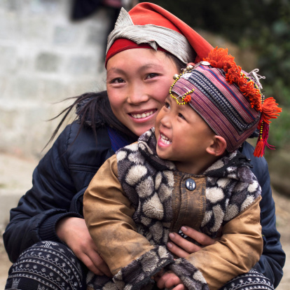 Happy Hmong woman and child smiling, sitting outside their house at Giang Ta Chai village near the hill town of Sa Pa, Lao Cai Province, North Vietnam.