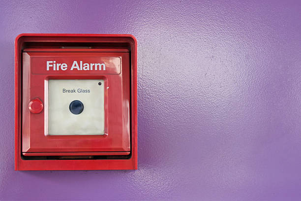 Red box of fire alarm on violet wall Red box of fire alarm with black button on violet background. emergency break glass box stock pictures, royalty-free photos & images
