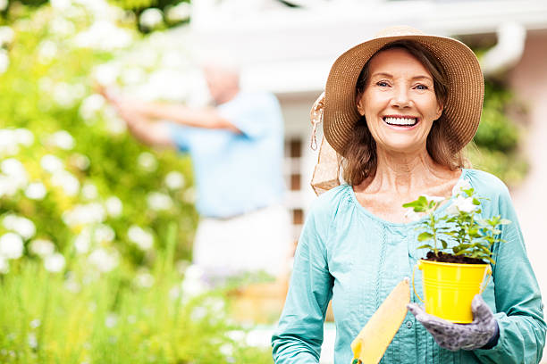 senior donna con vaso da fiori e giardinaggio pala mentre uomo - gardening couple senior adult ethnic foto e immagini stock