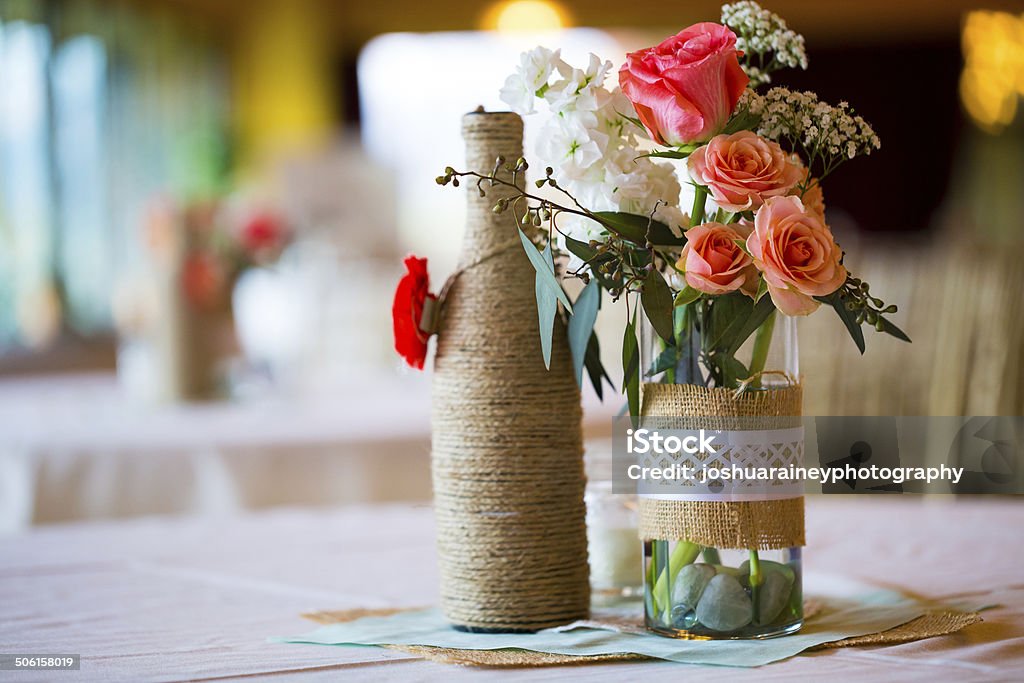Wedding Reception Table Centerpieces DIY wedding decor table centerpieces with wine bottles wrapped in burlap twine and rose flowers. DIY Stock Photo