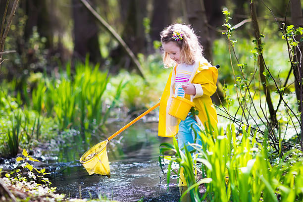 Child playing outdoors. Preschooler kid catching frog with colorful net. Little girl fishing in a forest river in summer. Adventure kindergarten day trip into wild nature, young explorer hiking and watching animals.