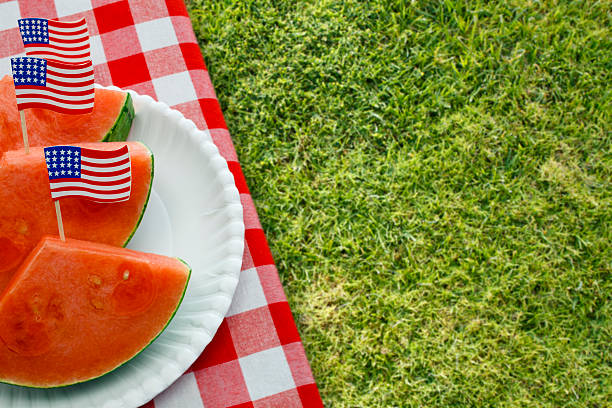 Slices of watermelon on a red checked picnic tablecloth with US flags in plated slices of watermelon for patriotic holiday picnics such as July Fourth, Memorial Day and Labor Day.