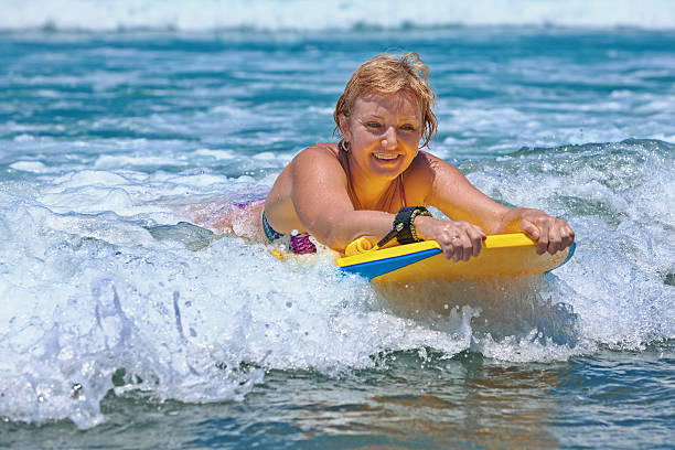 positif femme d'âge mûr avec son de surf sur les vagues de l'océan - senior adult surfing aging process sport photos et images de collection