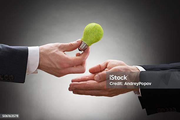 Businessman Giving Eco Light Bulb To Other Businessperson Stock Photo - Download Image Now