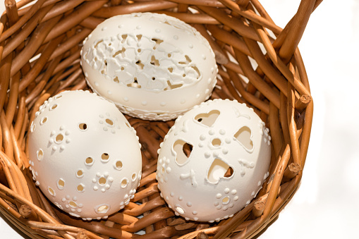 three perforated Easter eggs in wicker basket on white background