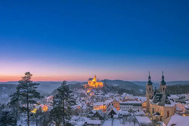 Elevated view over the beautiful village of Gößweinstein with it´s landmark Basilica and Burg Gössweinstein in the distance on a beautiful winter day at dusk. 
