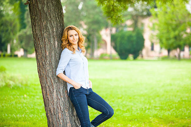 beautiful young woman standing next to a tree stock photo