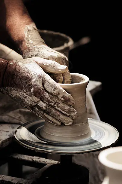 Pottery with unfired green ware. Potter's Hands turning a beaker on a potter's wheel. Ceramics.