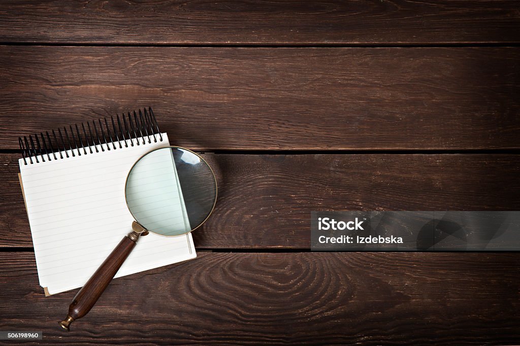 notebook with a magnifying glass on a wooden background Detective Stock Photo