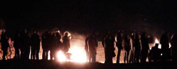 People Standing By Burning Campfire In The Night