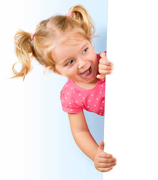 Smiling little girl looking behind a white board blonde girl emerges from a billboard peeking stock pictures, royalty-free photos & images