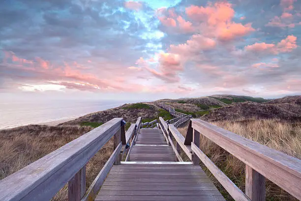 Wooden footpath through dunes at the North sea beach in Germany. sunset