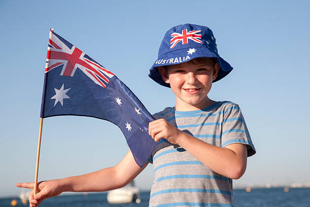 A cute Australian boy holding up an Australian flag at the beach.