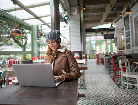 Asian woman working on a laptop at a restaurant and dressed in winter clothes