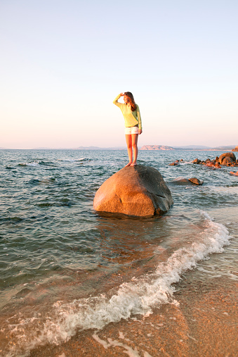 Fifteen years old girl looking ahead from a boulder in the beach. Taken at Sardinia.