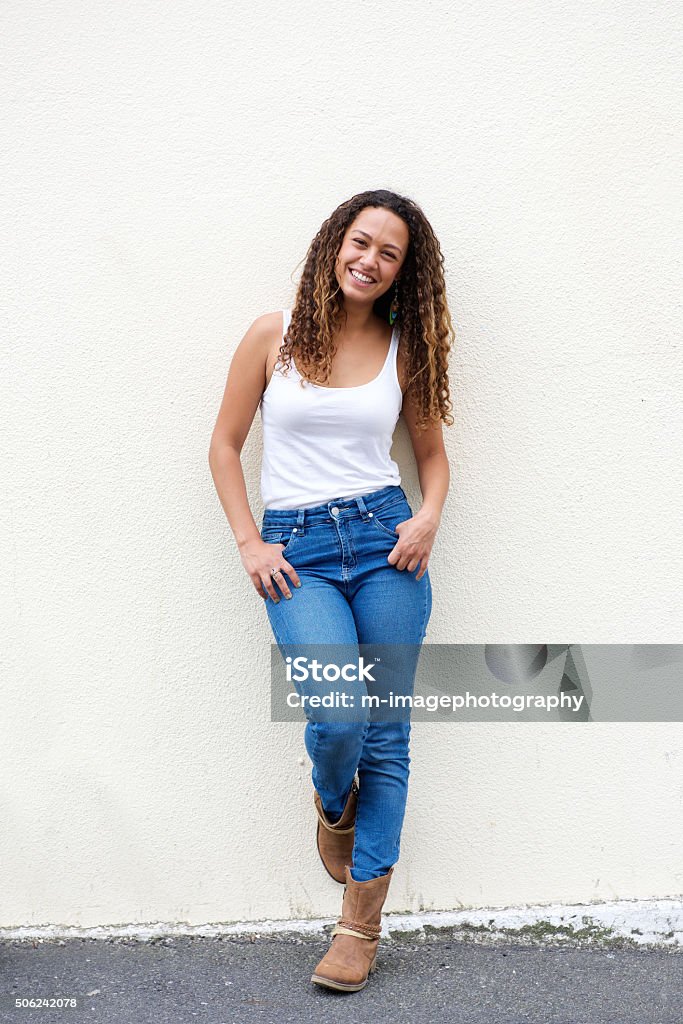 Smiling young woman posing outdoors Full length portrait of smiling young woman leaning against a wall looking at camera. Women Stock Photo
