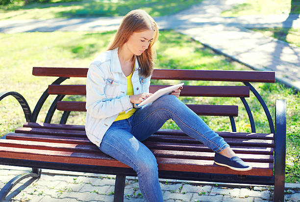 istock Young woman using tablet pc on bench in city park 506244902