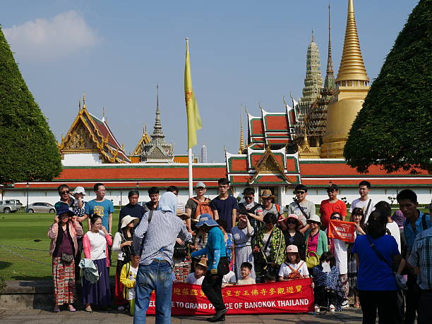 Tourists and Temple of the Emerald Buddha, Bangkok Bangkok, Thailand – January 22, 2016: Tourists take group photos in Wat Phra Kaew. Wat Phra Kaew and Grand Palace are one of the most popular tourist destinations in Bangkok.  :  theravada photos stock pictures, royalty-free photos & images