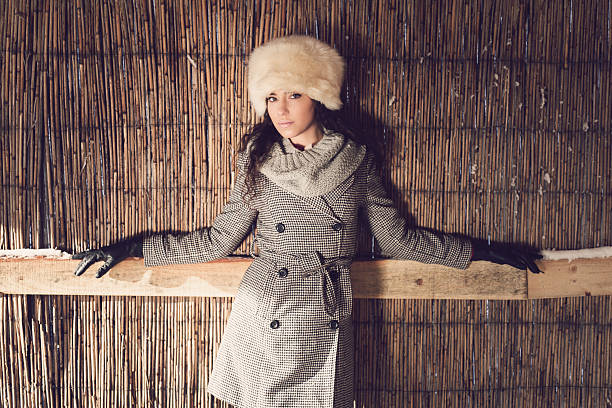 Fashion portrait of a beautiful young woman posing on a reed wall.