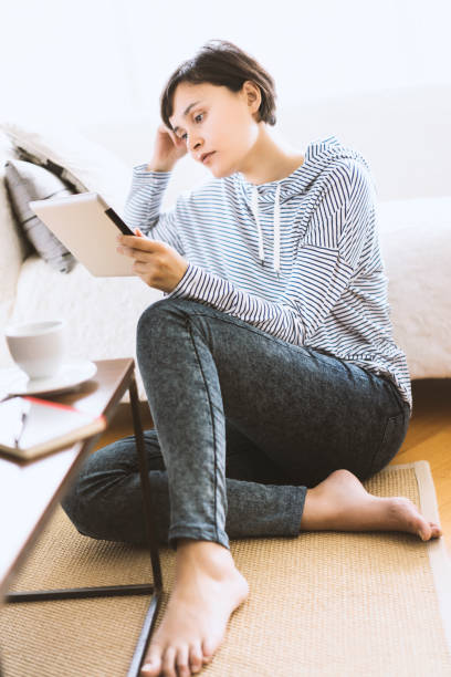 istock Young woman sitting on the floor using tablet pc 506251356