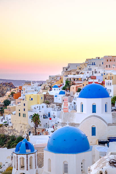 malerischer blick auf den farbenfrohen häusern und die blauen kuppeln ein sonnenuntergang - travel locations cyclades islands santorini vertical stock-fotos und bilder