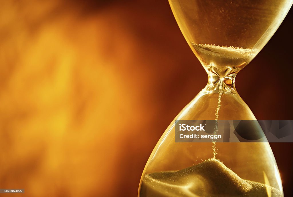 Sand passing through the bulbs of an hourglass Sand passing through the glass bulbs of an hourglass measuring the passing time as it counts down to a deadline or closure on a yellow background with copyspace Activity Stock Photo