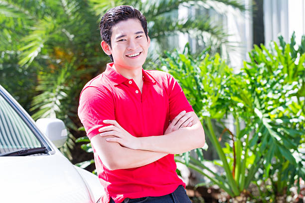 Asian man standing in front of new car