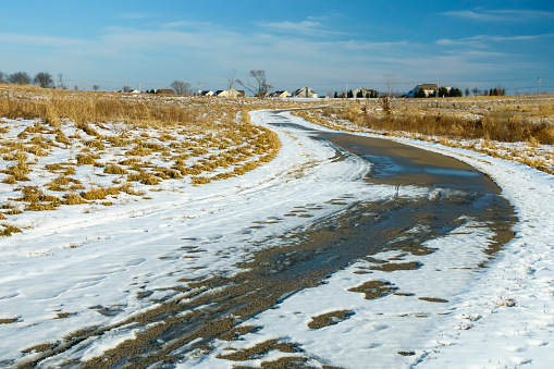 Wide trail with melting snow in an S-curve across a nature preserve near a suburban neighborhood, January in northern Illinois, USA, for seasonal, recreational, or environmental themes