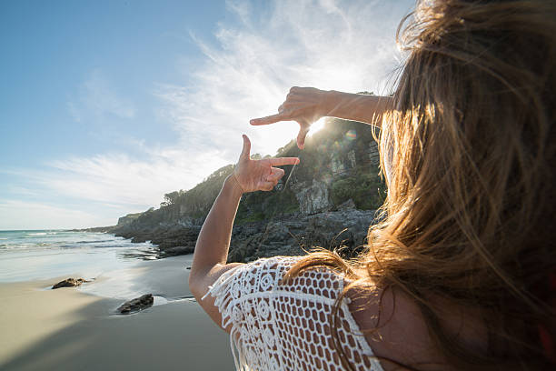 istock Young woman on beach makes finger frame to the sun 506297438