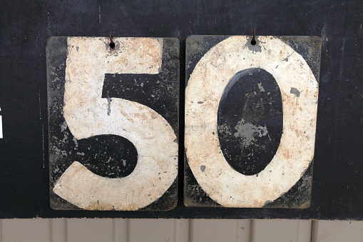 A digital photograph of the number fifty (50) made up from the numbers of an old cricket scoreboard. The numbers are white and the back boards are black.