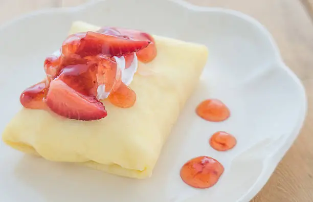 Strawberry crepe cake in white dish placed on wooden floor.Focus strawberry top cake.
