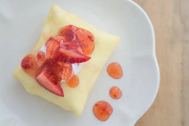 Strawberry crepe cake in white dish placed on wooden floor.Focus strawberry top cake.