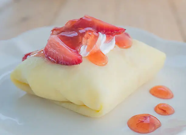 Strawberry crepe cake in white dish placed on wooden floor.Focus strawberry top cake.