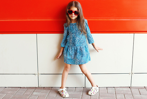 Beautiful little girl model wearing a leopard dress and sunglasses over colorful red background