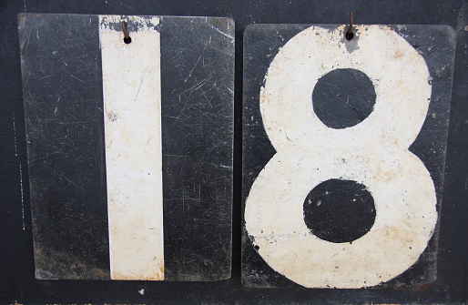 A digital photograph of the number eighteen (18) made up from the numbers of an old cricket scoreboard. The numbers are white and the back boards are black.