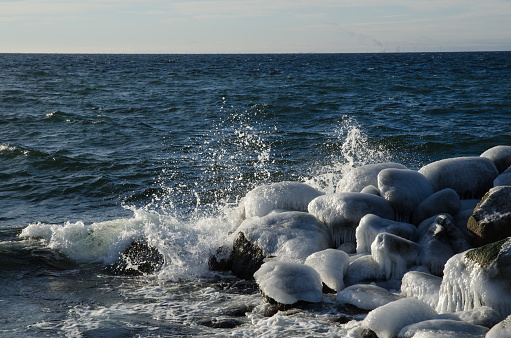 Splashing waves at ice covered rocks by a coast with a deep blue water