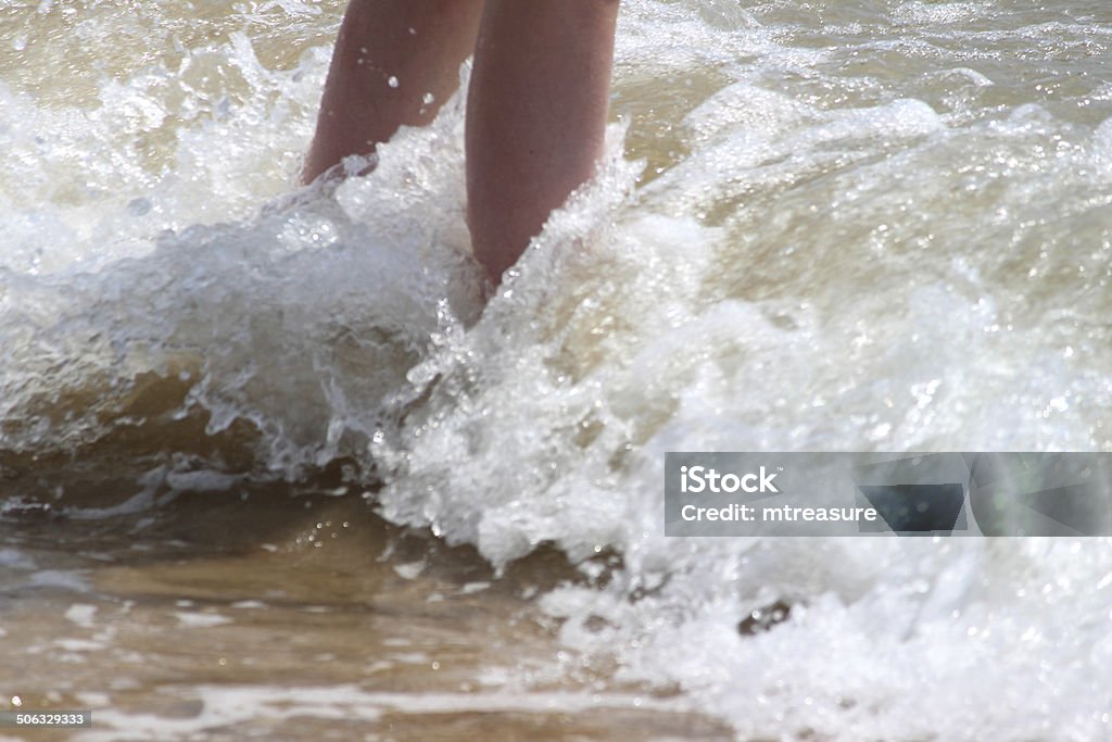 Girl paddling in sea waves, legs, water, barefoot, seaside beach Photo showing a young girl paddling in the gentle sea waves and curling her toes upwards, showing her barefoot with the legs partly in the tide / water and the sea splashes over them.  The girl was having lots of fun at the seaside, playing on the beach during her sunny summer holiday. Ankle Deep In Water Stock Photo