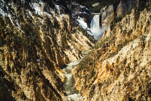 A panoramic landscape view of Lower Yellowstone Falls in Yellowstone National Park.  Snow still borders some of the rivers edge.  Horizontal image with copy space.