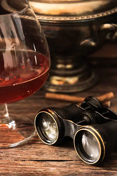 Photo of glass of cognac with binoculars and blue stained-glass candle