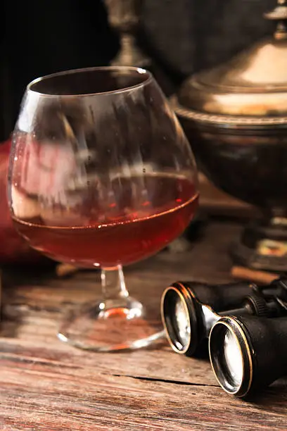 Photo of glass of cognac with binoculars and blue stained-glass candle