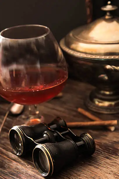 Photo of glass of cognac with binoculars and blue stained-glass candle