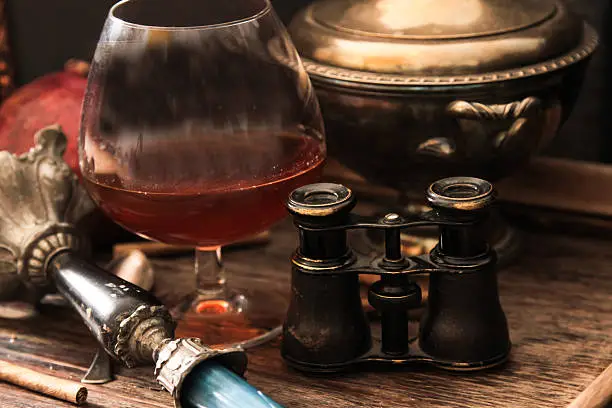 Photo of glass of cognac with binoculars and blue stained-glass candle