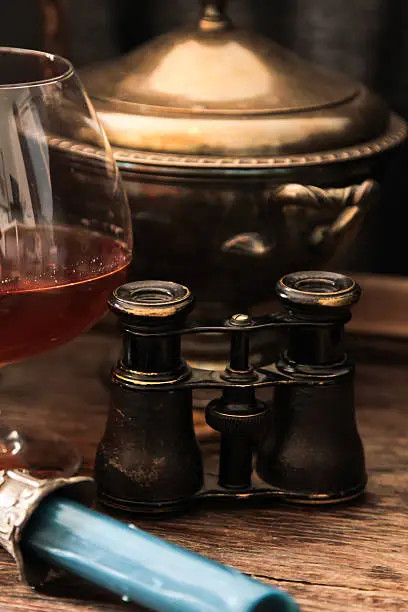 Photo of glass of cognac with binoculars and blue stained-glass candle