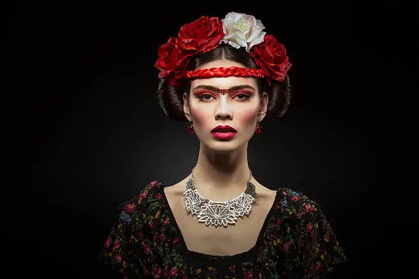 Beautiful young woman with bright red make up looking like Frida Kahlo. Over black background. Copy space.