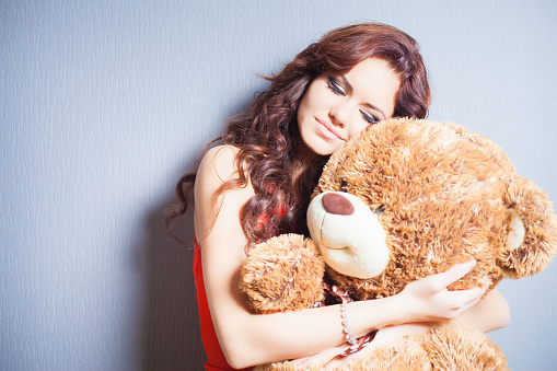 Happy woman received a teddy bear. Blue background. Her beautiful eyes looking at camera. Concept of holiday, birthday, World Women's Day or Valentine's Day, 8 March. Copy space