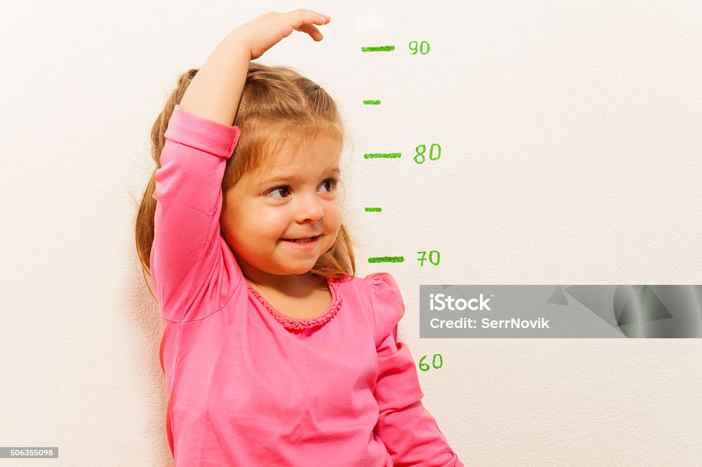 Height measurement by little girl at the wall Funny girl is measuring her height with painted graduations on the wall with her hand Child Stock Photo