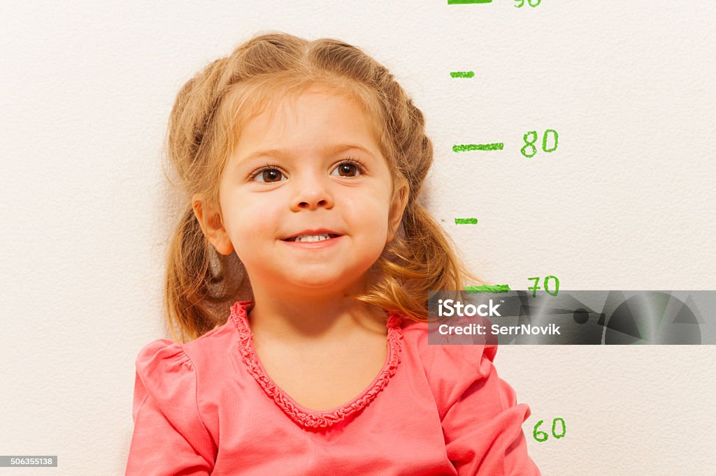 Little girl measuring height against wall in room Smiling little girl is measuring her height against the painted green height chart Growth Stock Photo