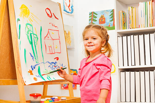istock Cute girl is drawing using a brush at easel 506355222